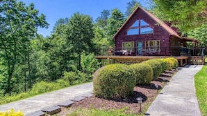 A log cabin with a porch, surrounded by well-maintained hedges and a pathway leading to the entrance. - …STUNNING Luxury 3BD Lodge! …HOT TUB/Games/VIEWS!… (Pigeon Forge)