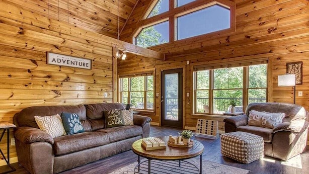 A cozy cabin interior with a brown leather sofa, a round coffee table, and a wooden floor. - …STUNNING Luxury 3BD Lodge! …HOT TUB/Games/VIEWS!… (Pigeon Forge)