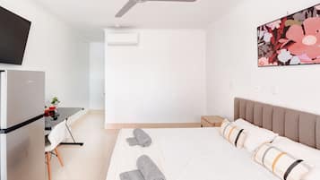 A hotel room with a bed, a desk, a chair, a television, and an air conditioning unit.