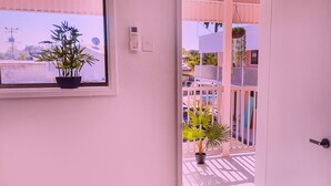 Une vue à travers une porte ouverte, donnant sur un balcon agrémenté de plantes en pot et muni d’une balustrade.