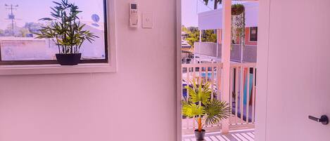 A view through an open door to a balcony with potted plants and a railing.