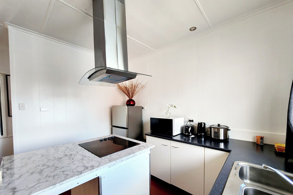 Una cocina moderna con armarios blancos, una campana extractora de acero inoxidable, encimera de mármol y hervidor eléctrico negro.