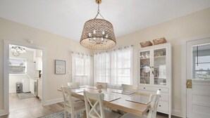 Un comedor con una mesa de madera, sillas blancas, un tapete estampado y una lámpara colgante.