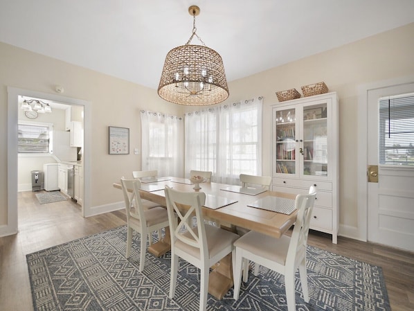 Un coin repas avec une table en bois, des chaises blanches, un tapis à motifs et un luminaire suspendu.