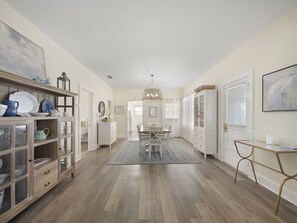 Un hall spacieux doté d’un plancher en bois, un coin repas agrémenté d’un lustre, et un buffet blanc aux portes en verre.