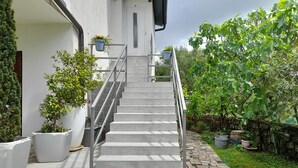 Una escalera que conduce a una puerta blanca, rodeada de plantas en macetas y un jardín.