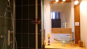 Un bagno con un lavandino a forma di coppa in vetro, uno specchio sopra e una cabina doccia rivestita di piastrelle nere.