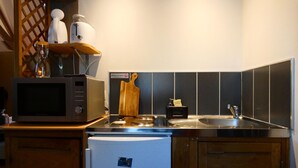 Una cucina compatta con forno a microonde, frigorifero, lavandino e tagliere in legno.