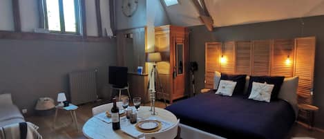 Una habitación con una cama, una mesa de comedor con sillas, un reloj y una ventana.