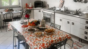 Una cocina con armarios blancos, una estufa a gas, un tostador y una mesa de comedor dispuesta con comida.