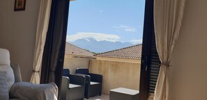 Un balcon agrémenté de meubles en osier, une vue sur les montagnes et un toit recouvert de tuiles.