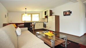 A compact living space with a sofa, a glass coffee table, a dining area with a chair, and a kitchen with cabinets and appliances.