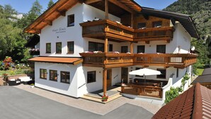 A two-story building with wooden balconies, a covered outdoor seating area, and a mountain backdrop.