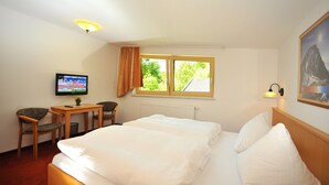 A hotel room with two beds, a TV, a desk with a chair, a window with curtains, and a lamp.