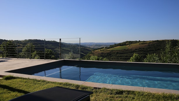 A rectangular infinity pool with clear blue water, surrounded by a concrete deck and a metal fence.