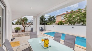 A glass table with chairs and a bottle of orange juice, a swimming pool, and a view of a building with trees. - Gorgeous home in Betiga (Betiga)