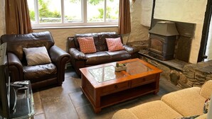 A cozy living room with leather sofas, a wooden coffee table, and a stone fireplace. - Peaceful spacious cottage close to mountain walks and beaches (Machynlleth)