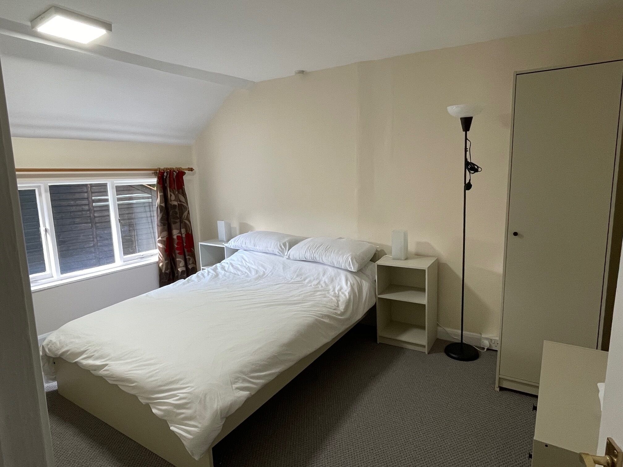 A bedroom with a single bed, a bedside table, a nightstand, a floor lamp, and a wardrobe.