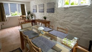A dining area with a glass table, wooden chairs, and a stone wall. - Peaceful spacious cottage close to mountain walks and beaches (Machynlleth)