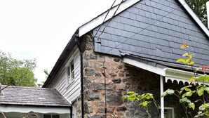 A stone house with a sloped roof, a wooden fence, and a garden with various plants and flowers. - Peaceful spacious cottage close to mountain walks and beaches (Machynlleth)