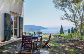 An outdoor patio with a table and chairs overlooking a scenic view of the sea and hills. - Cozy home in San Piero In Campo with WiFi (San Piero In Campo)