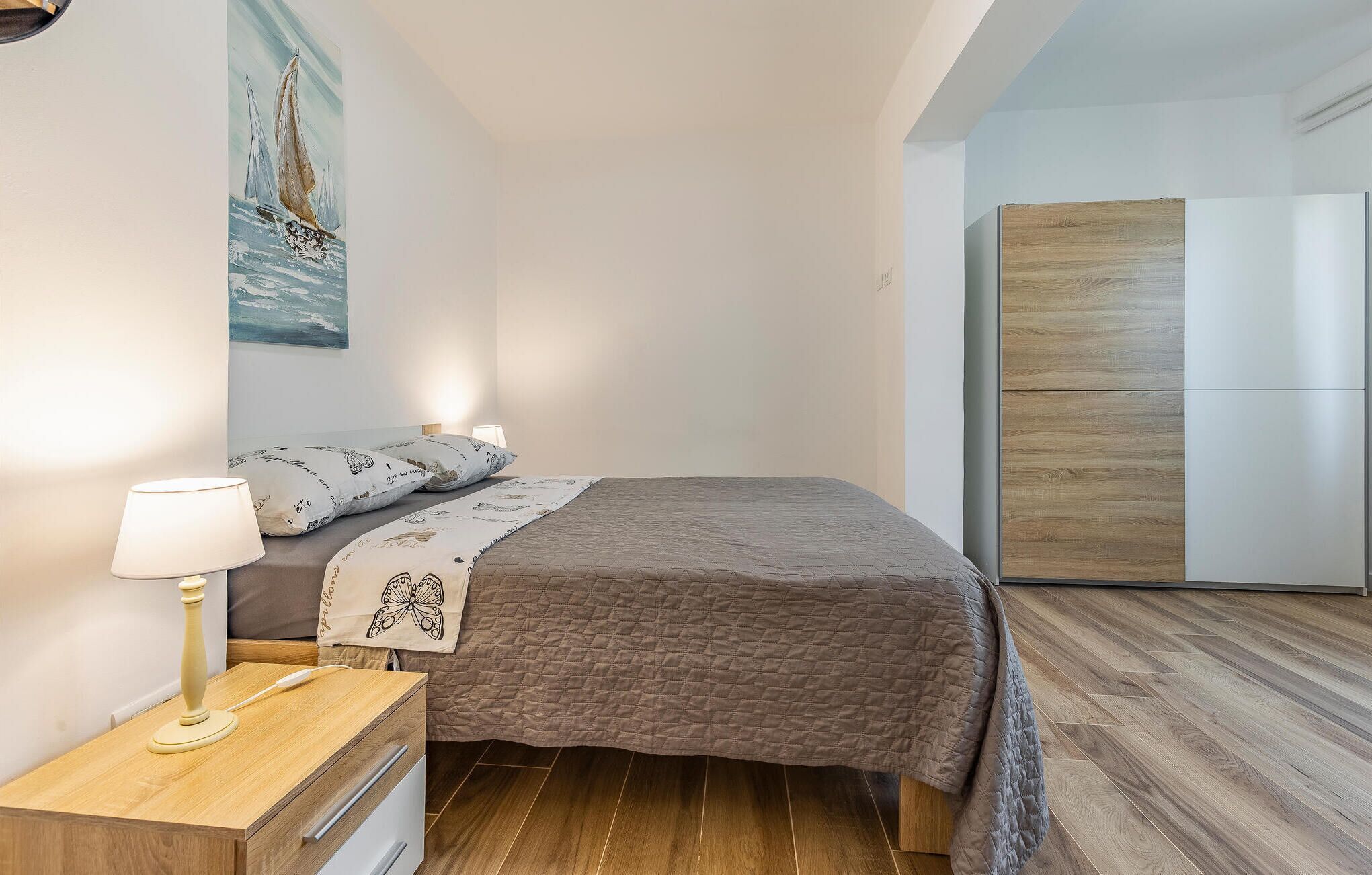 A bedroom with a bed, bedside tables, a lamp, a painting, and a wardrobe.