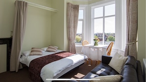 Ein Schlafzimmer mit einem Bett, einem Sofa, einem Tisch mit einer Vase und einem Fenster mit Vorhängen.