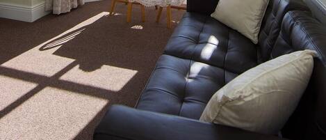 Ein Eckzimmer mit Erkerfenster, einer schwarzen Ledersofa, einem Tisch mit einer Vase und Vorhängen.
