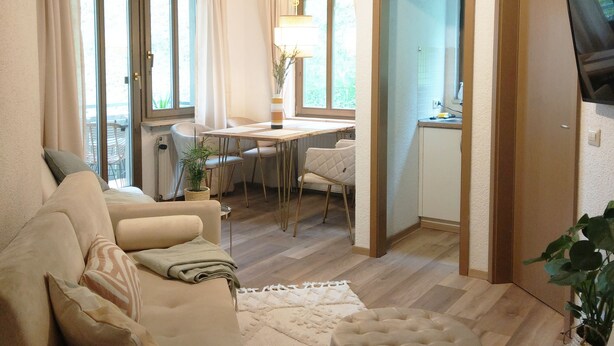 Una sala de estar con sofá, reposapiés y comedor con mesa y sillas.