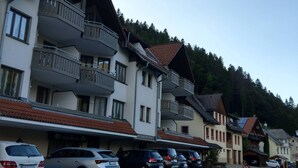 Una hilera de edificios de varios pisos con balcones, autos estacionados y montañas al fondo.
