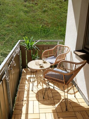 A wooden deck with a round glass table and two wicker chairs, a potted plant, and a string of light bulbs.