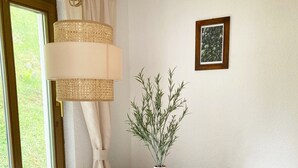 Un comedor con una mesa de madera, sillas blancas, un jarrón con plantas y un cuadro en la pared.
