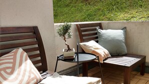Una terraza de madera con dos sillas de madera y una mesita, cada una con un cojín. Hay una planta en maceta sobre la mesa.