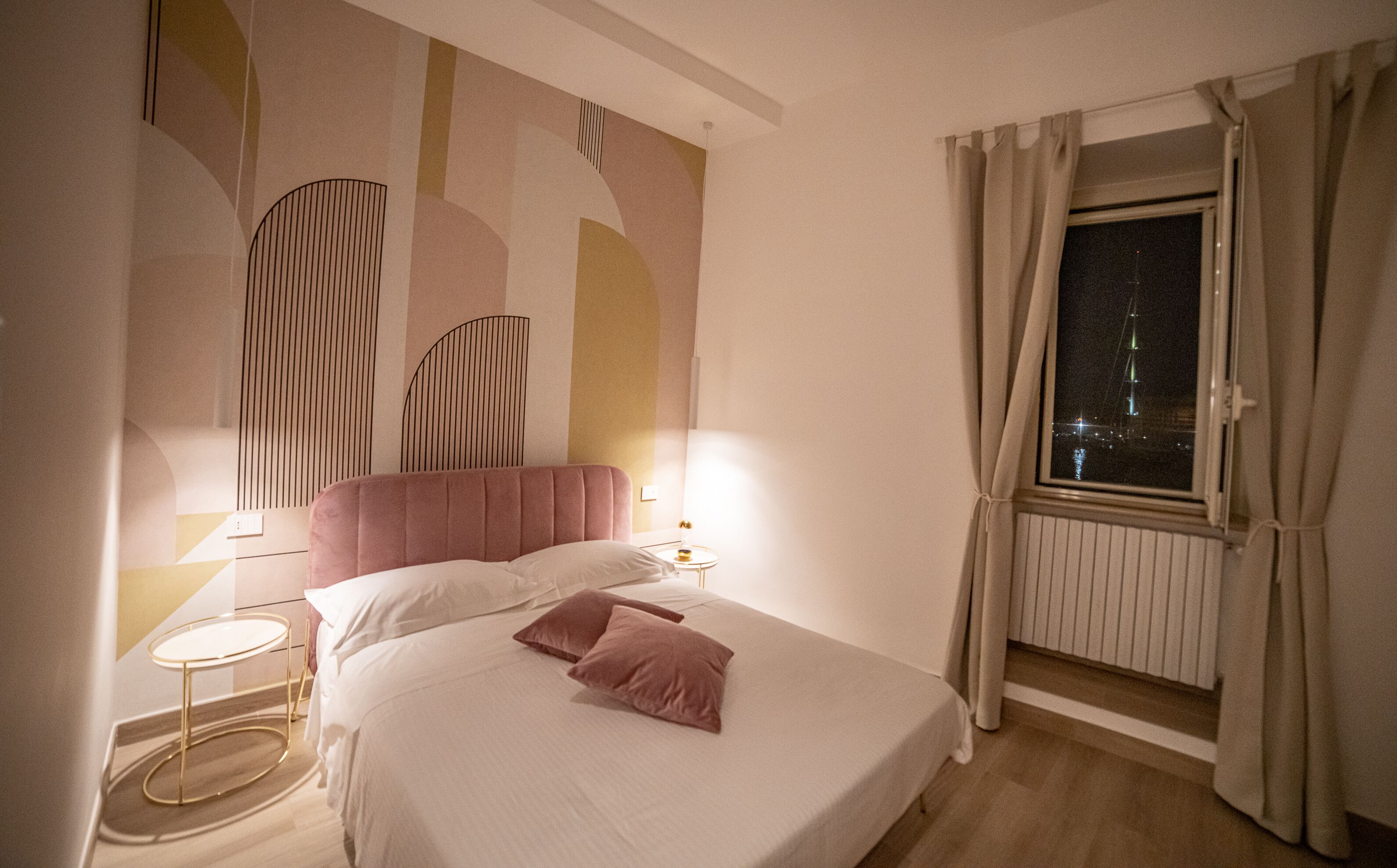 Una habitación de hotel con cama, mesitas de noche, ventana con cortinas y una pared decorada con arte abstracto.