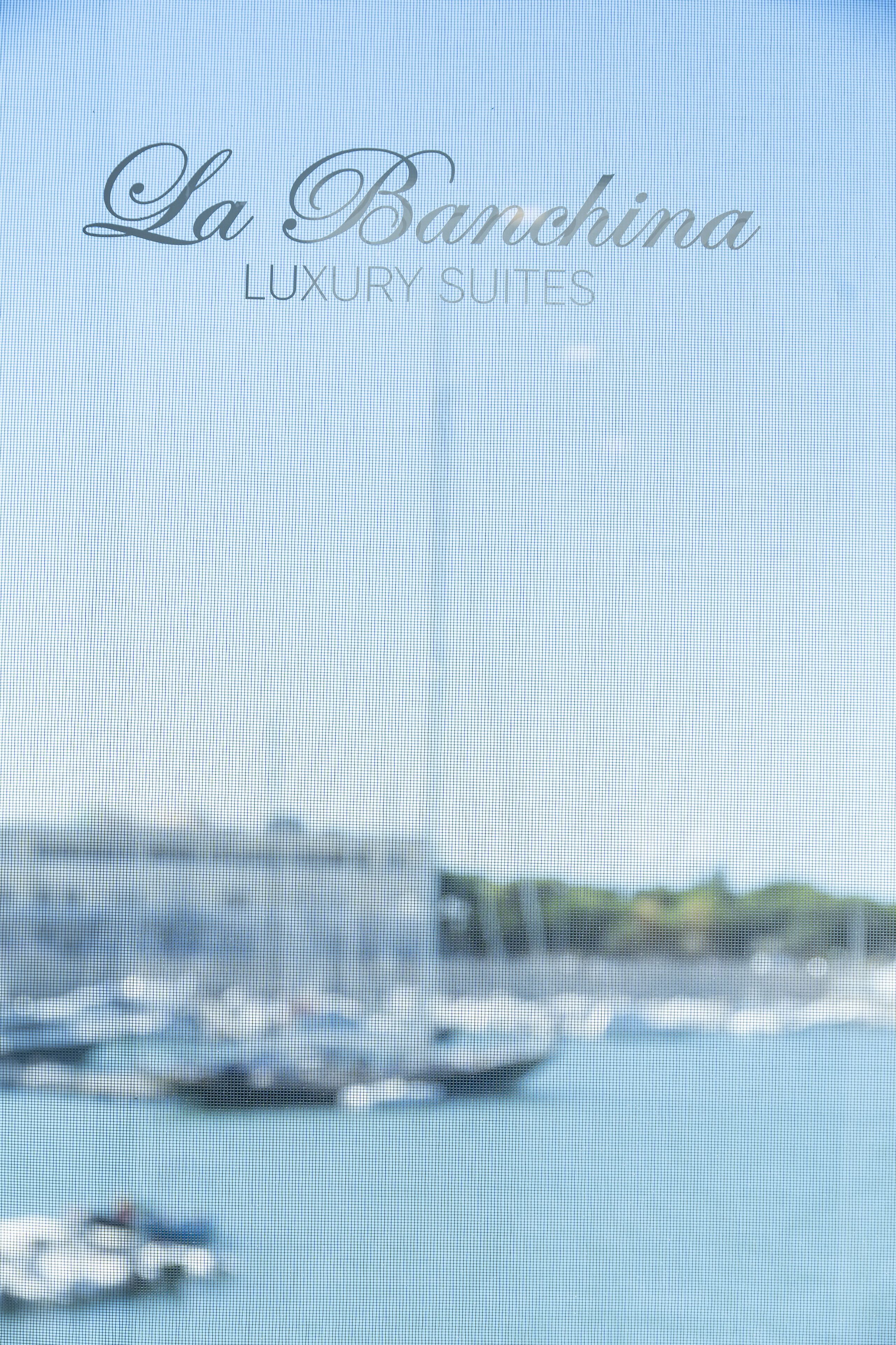 A blurred view of a marina with boats, and the text "La Banchina Luxury Suites" is visible.