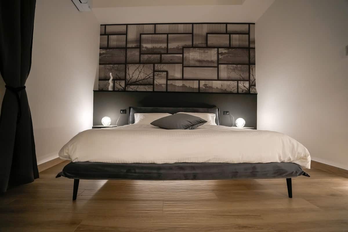 A modern bedroom with a large bed, a decorative wall panel, and bedside lamps.