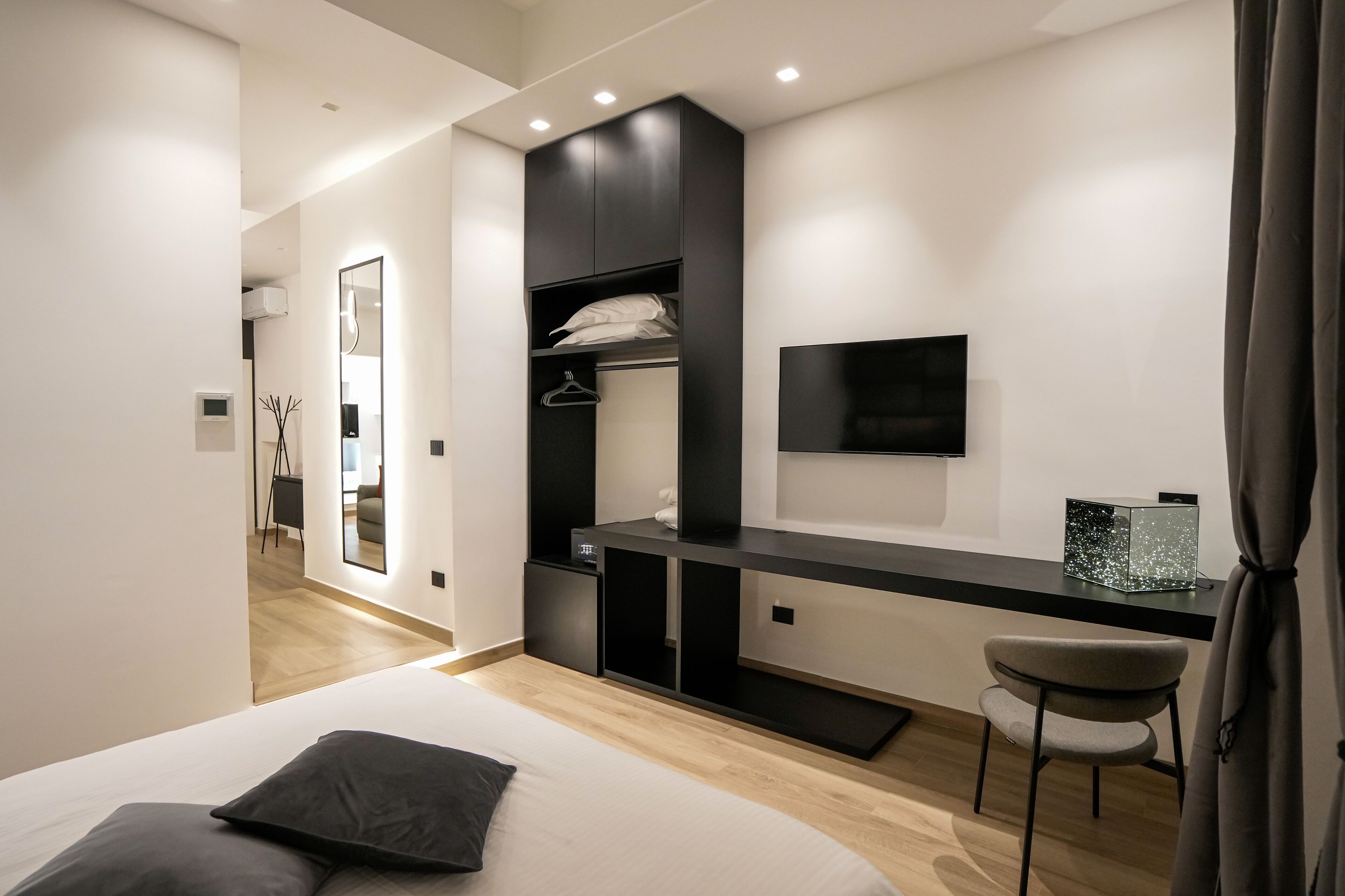 A modern bedroom with a bed, a desk, a chair, a TV, and a wardrobe.