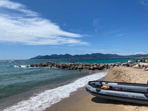 A beach with a police boat labeled "POLICE MUNICIPAL" and a rocky breakwater.