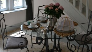 A dining area with a glass table, metal chairs, a vase of flowers, and a staircase in the background. - The Orangerie in the grounds of Chateau St Justin (Saint-Justin)