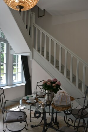 Un coin repas avec une table en verre, des chaises en métal, un vase de fleurs et un escalier en arrière-plan.