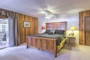 Une chambre avec un lit en bois, un ventilateur de plafond, une table de chevet avec une lampe et une fenêtre avec des rideaux.