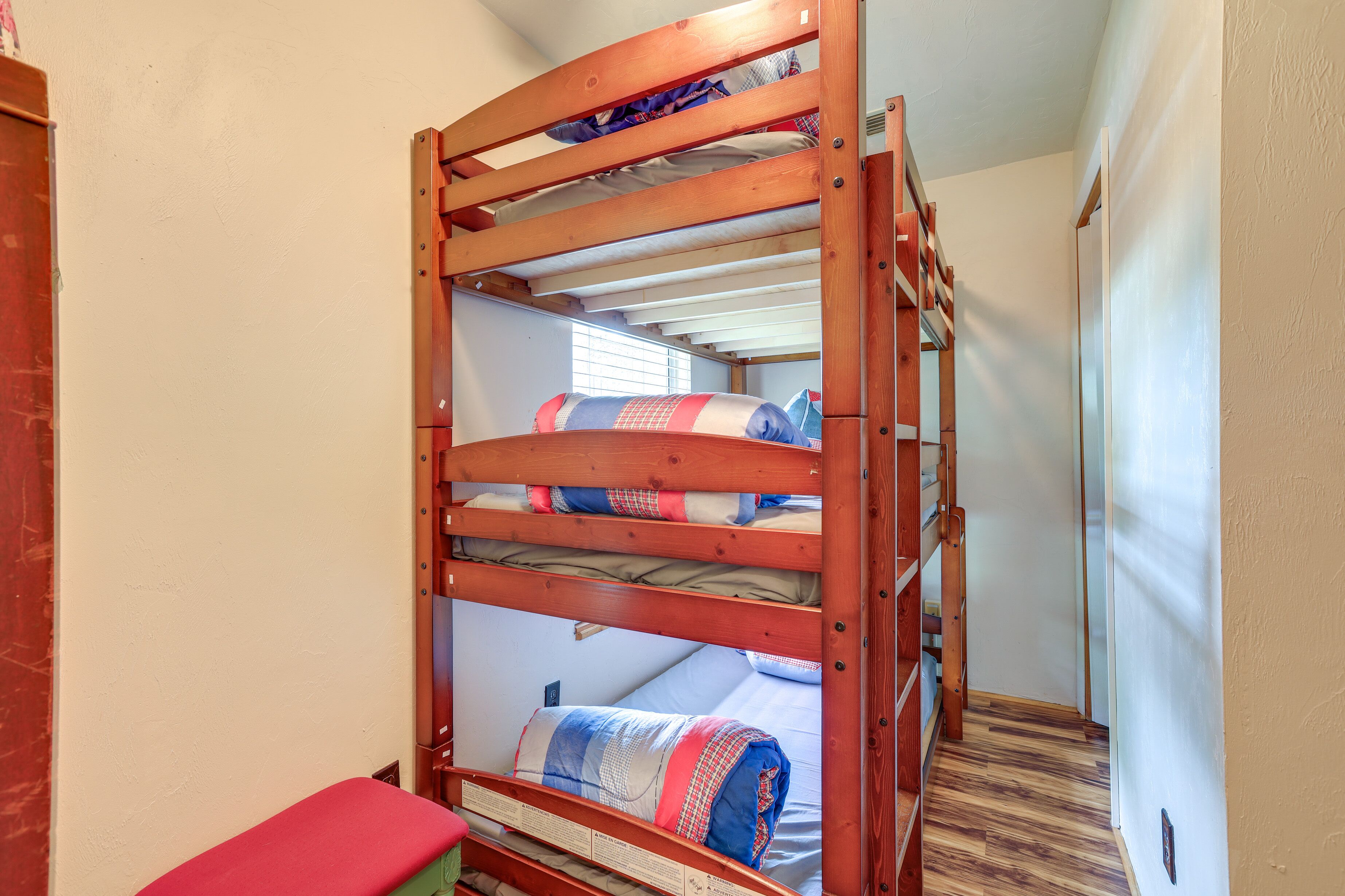 Ein Stockbett mit Holzrahmen, eine rote Bank und eine gemusterte Decke.