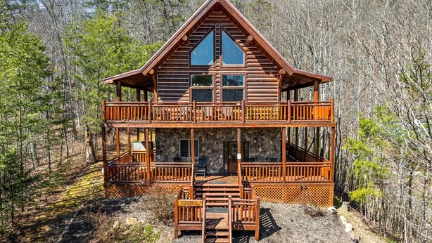 A two-story log cabin with a balcony, surrounded by forest. - LOG CABIN★SECLUDED AUGUST SPECIALS★HOT TUB★GAME ROOM★CONVENIENT★FIRE PIT (Sevierville)