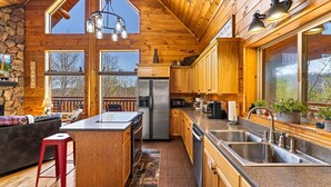 A spacious kitchen with wooden cabinets, a stainless steel refrigerator, and a large island with a sink. - LOG CABIN★SECLUDED AUGUST SPECIALS★HOT TUB★GAME ROOM★CONVENIENT★FIRE PIT (Sevierville)