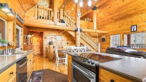A wooden cabin interior with a kitchen, dining area, and a staircase leading to a loft. - LOG CABIN★SECLUDED AUGUST SPECIALS★HOT TUB★GAME ROOM★CONVENIENT★FIRE PIT (Sevierville)