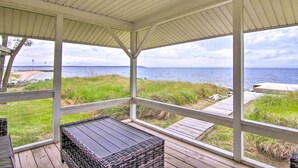 En overdækket terrasse med fletningsmøbler og udsigt til stranden og vandet.