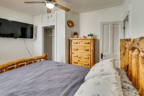 A bedroom with a bed, wooden headboard, a dresser, a television mounted on the wall, and a ceiling fan.