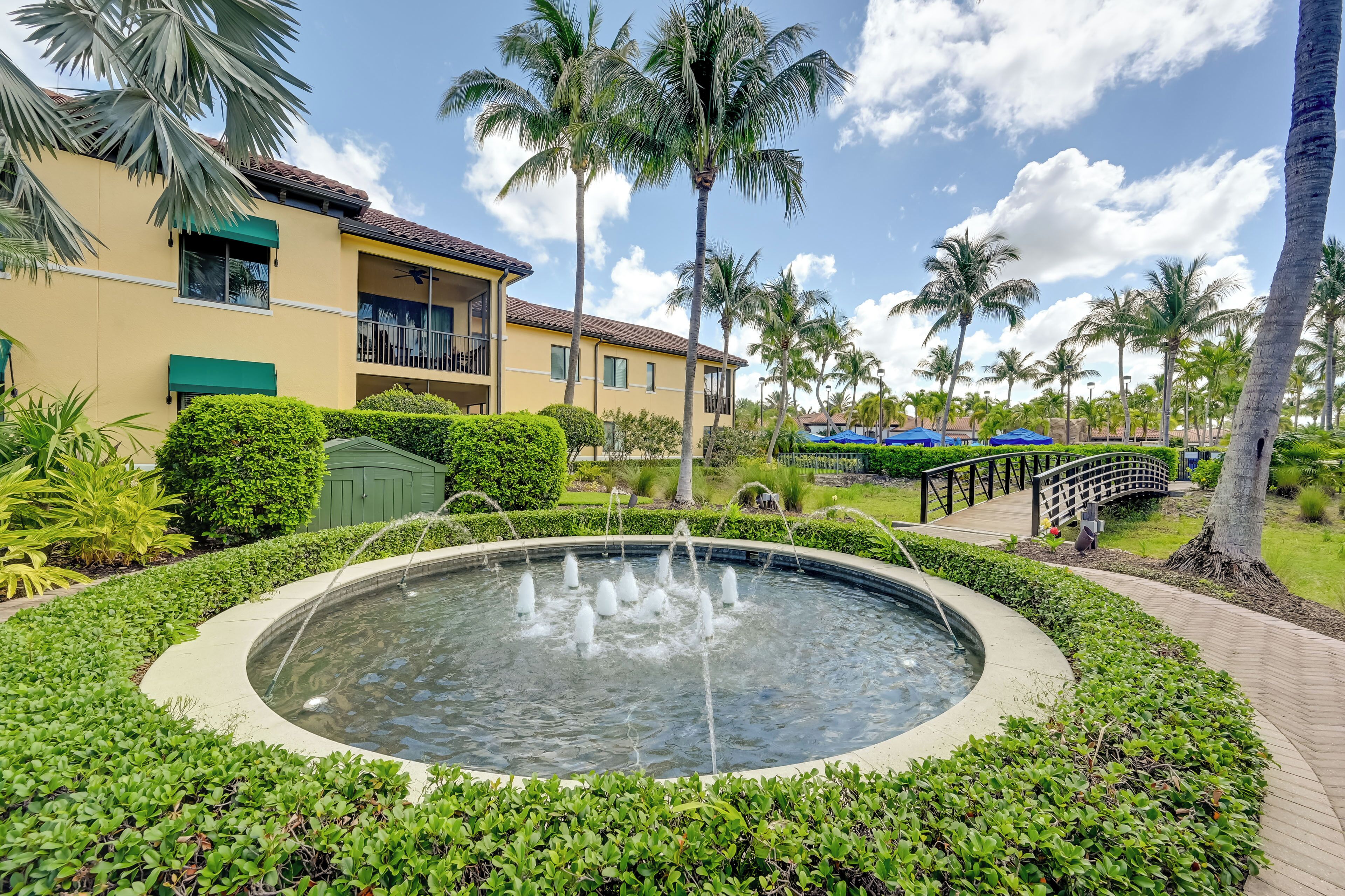 A courtyard with a circular water feature, palm trees, and a building with balconies.