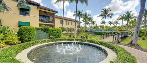 A courtyard with a circular water feature, palm trees, and a building with balconies.