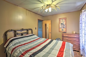 Een slaapkamer met een bed, een houten dressoir, een spiegel en een plafondventilator.
